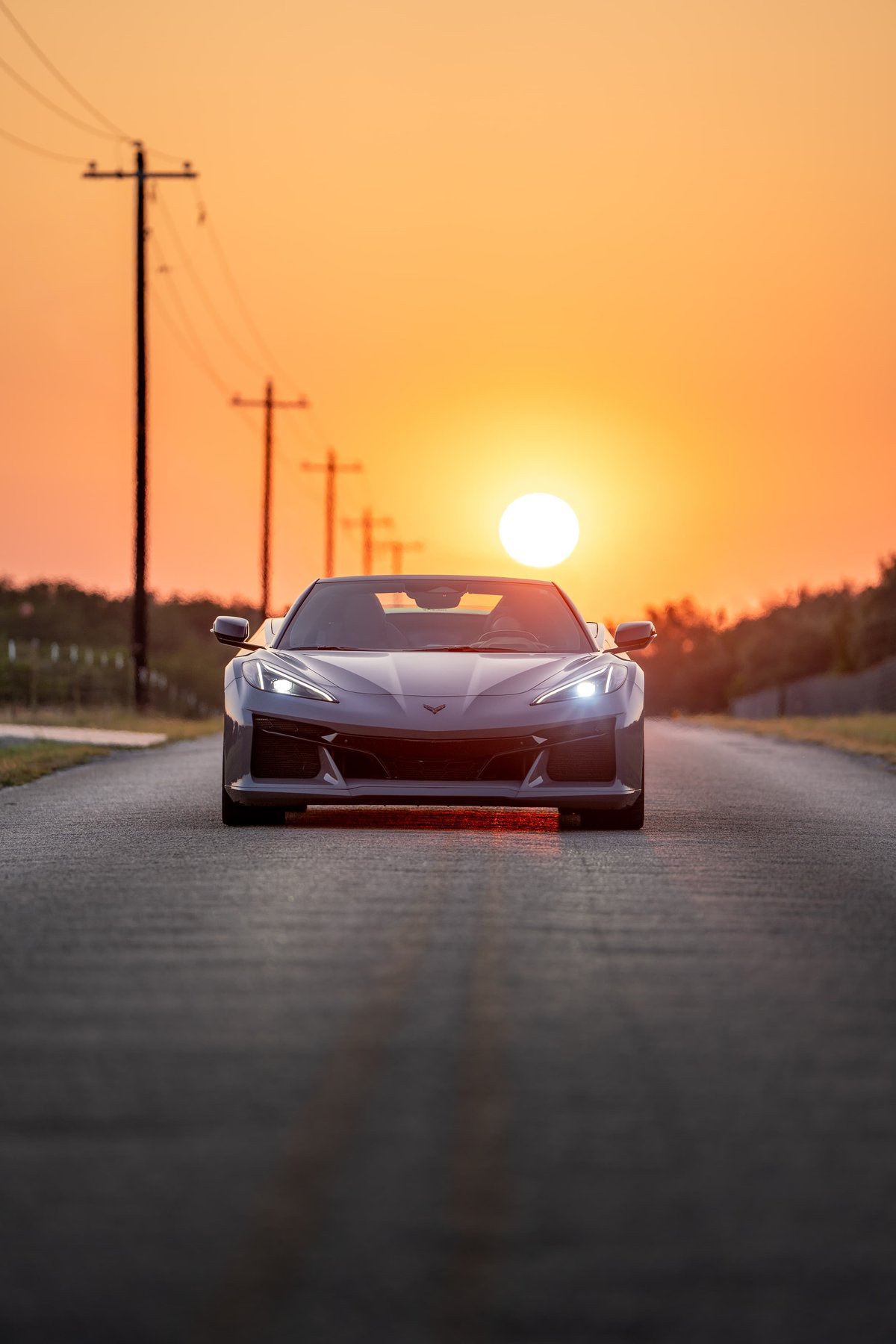Front view of a Sea Wolf Gray 2025 Chevrolet Corvette Z06 on a road at sunset.