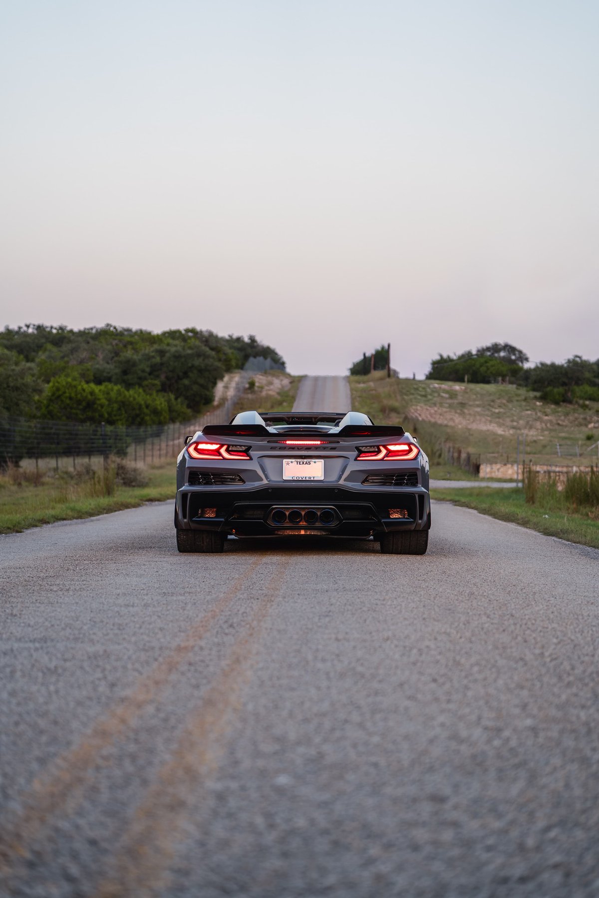 Rear view of a Sea Wolf Gray 2025 Chevrolet Corvette Z06 convertible on a rural road.