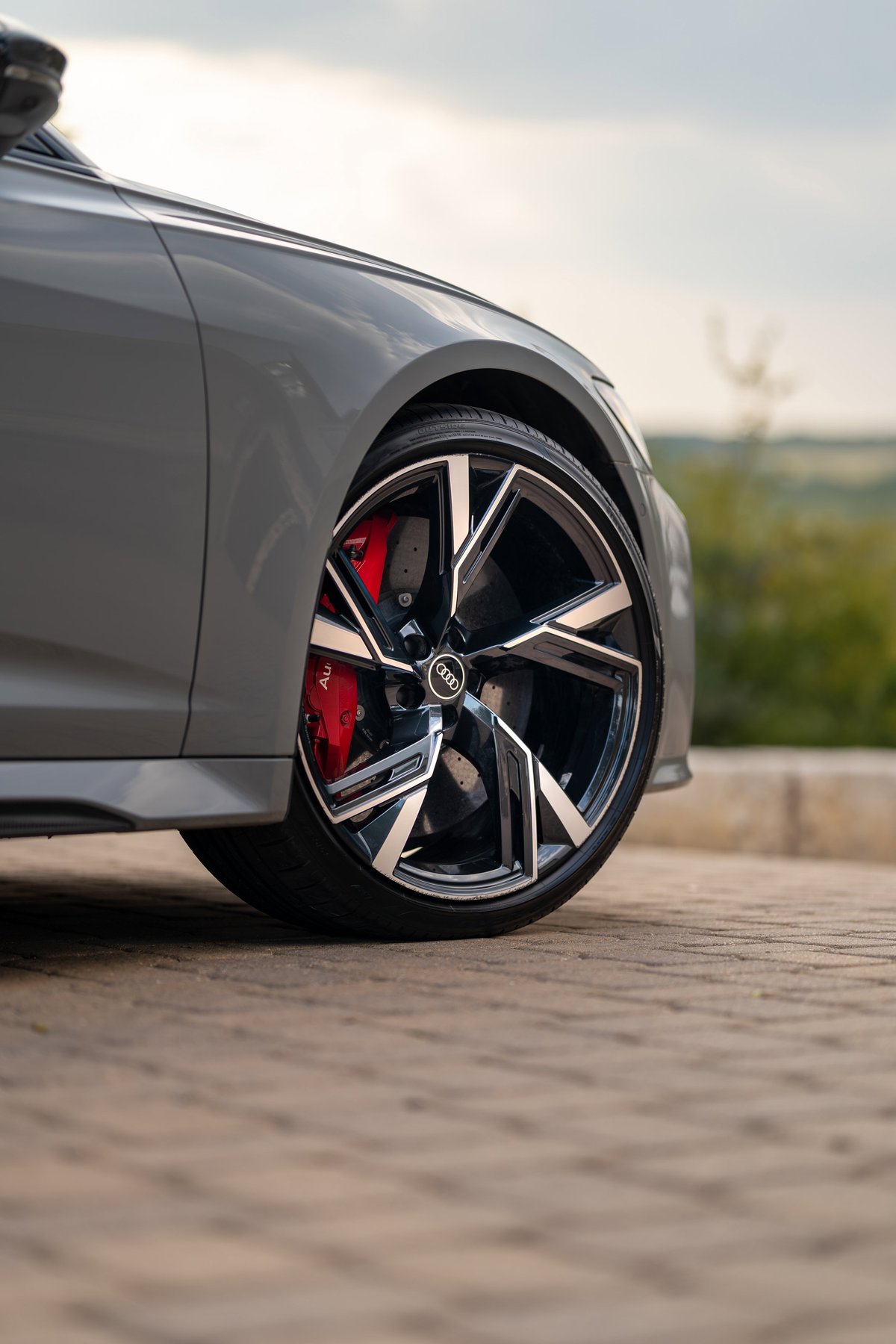 Close-up of a Nardo Grey 2022 Audi RS6 Avant's front wheel, featuring black and silver multi-spoke rims and red brake calipers.