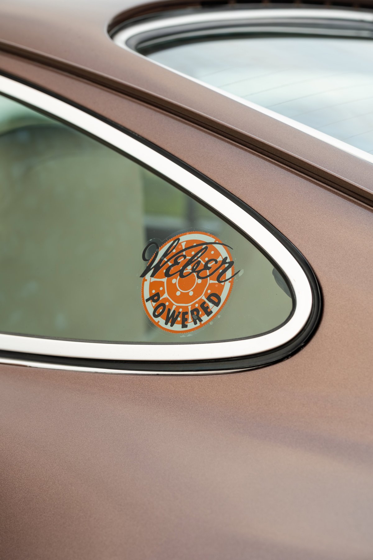 Detail of a 1975 Porsche 911 Carrera in Copper Brown Metallic with a "Weber Powered" sticker on the rear quarter window.