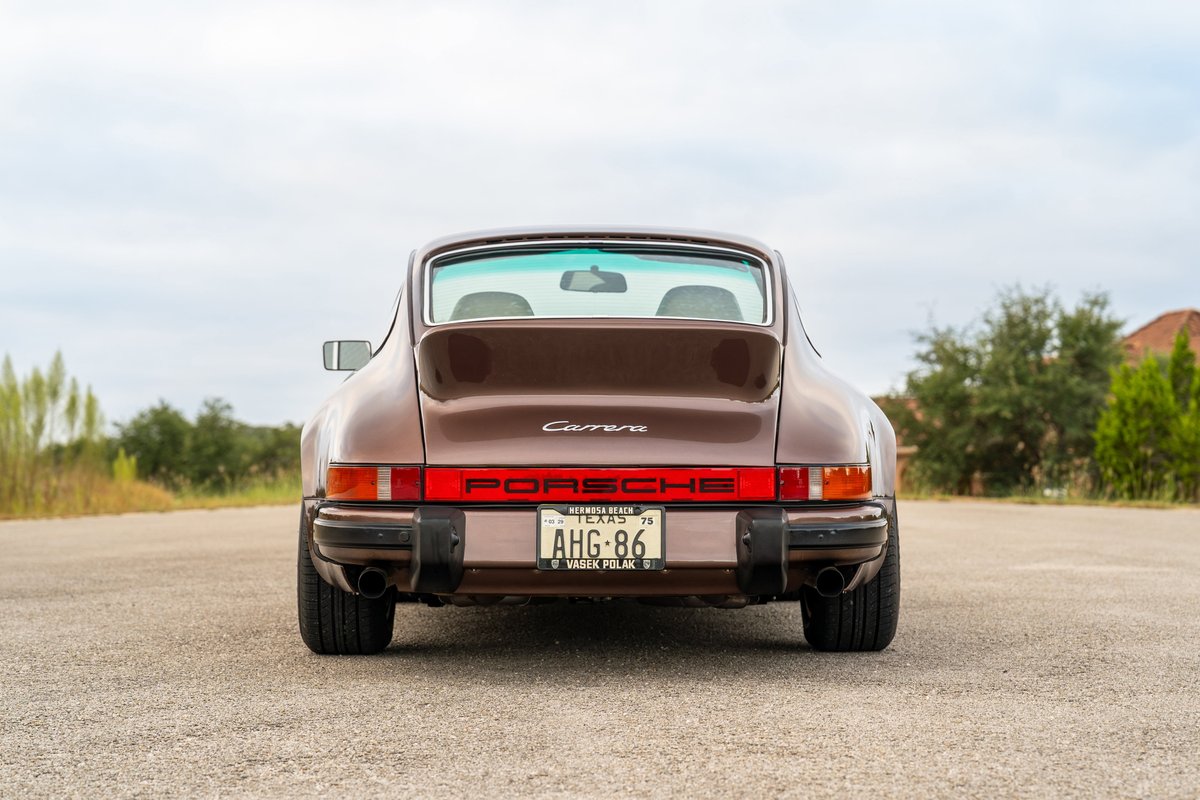 Rear view of a copper brown metallic 1975 Porsche 911 Carrera with black trim and dual exhaust pipes.