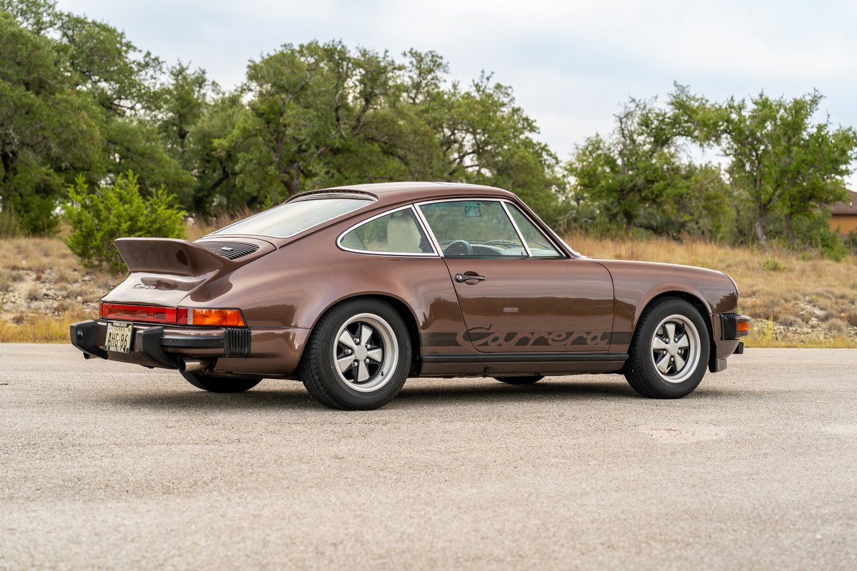A brown 1975 Porsche 911 Carrera with a ducktail spoiler and Fuchs rims.