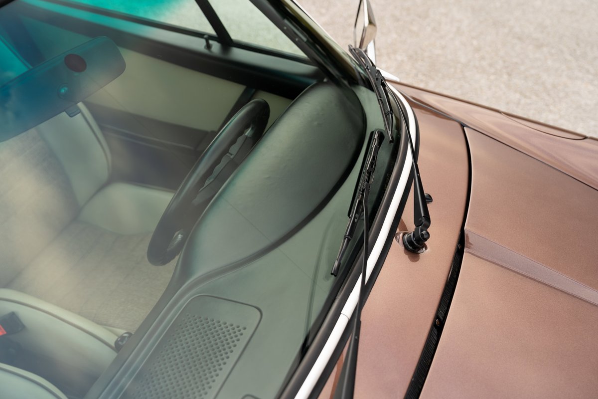 Close-up of a 1975 copper brown metallic Porsche 911 Carrera interior, showing windshield wipers and cream upholstery.