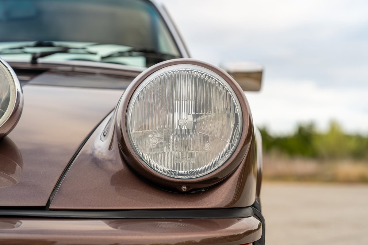 Front view of a copper brown metallic 1975 Porsche 911 Carrera's round headlight.