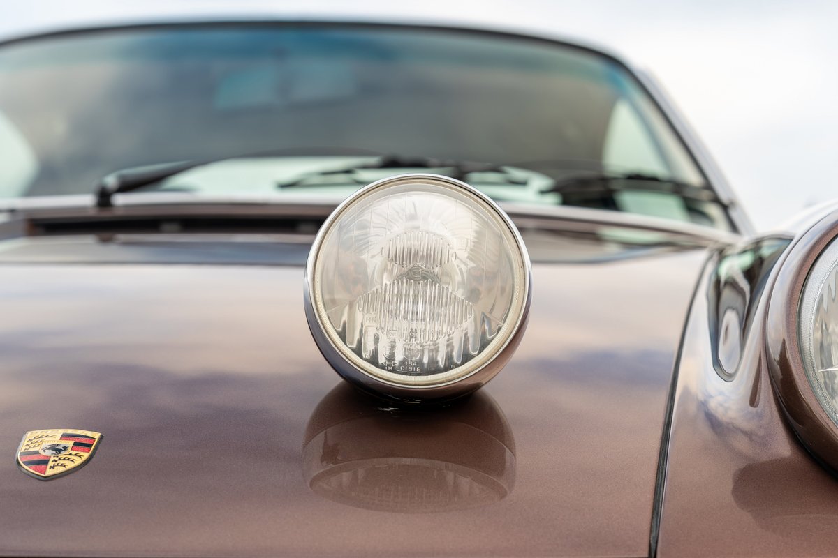Front view of a metallic copper brown 1975 Porsche 911 Carrera with chrome headlight trim and emblem.