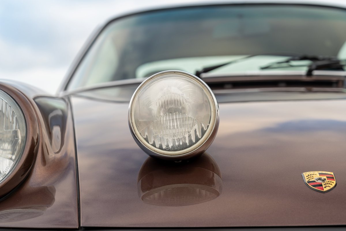 Close-up of a 1975 Porsche 911 Carrera in Copper Brown Metallic, featuring a fog light.