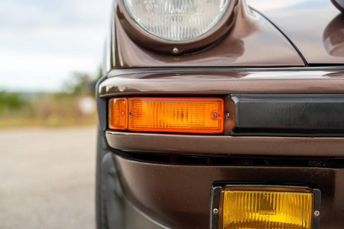 Front view of a 1975 Porsche 911 Carrera in Copper Brown Metallic, showing the amber turn signal and fog light.