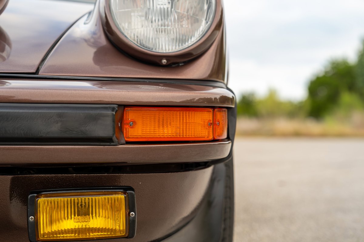 Close up of a copper brown 1975 Porsche 911 Carrera front bumper, turn signal, and headlight.