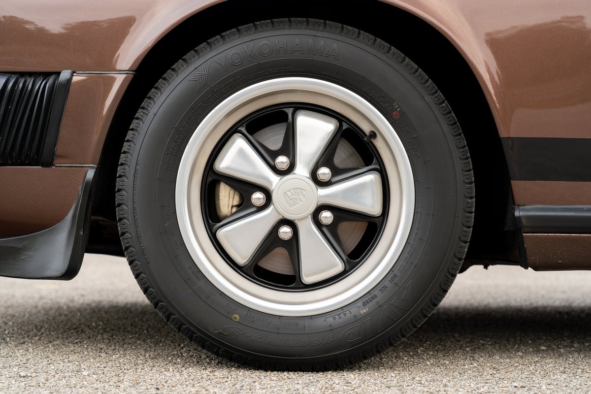 Close-up of a brown 1975 Porsche 911 Carrera's Fuchs rim and tire.