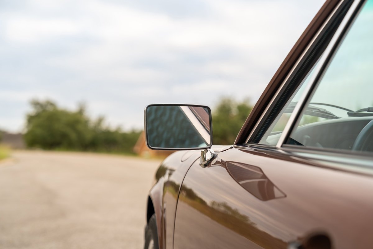 Close-up of a copper brown metallic 1975 Porsche 911 Carrera door and side mirror.