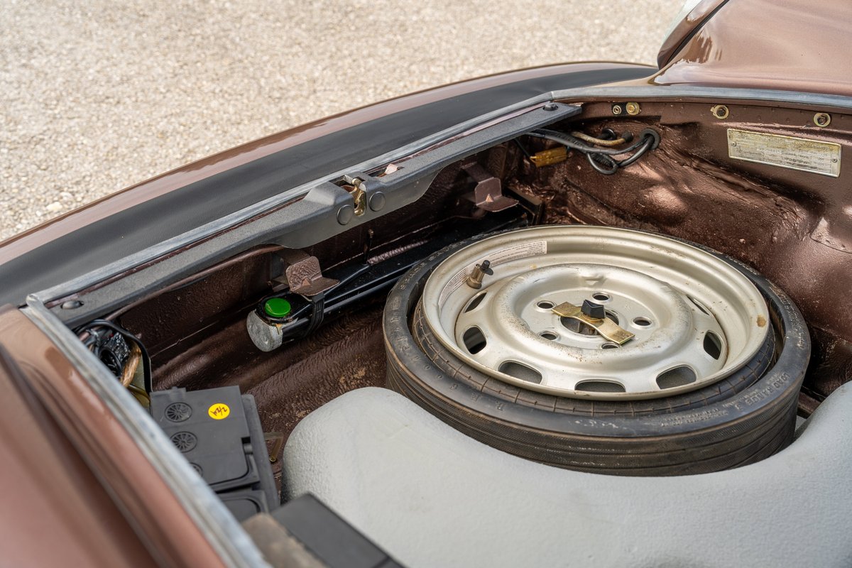 1975 Porsche 911 Carrera front trunk with spare tire, battery, and jack. Copper brown metallic exterior trim.