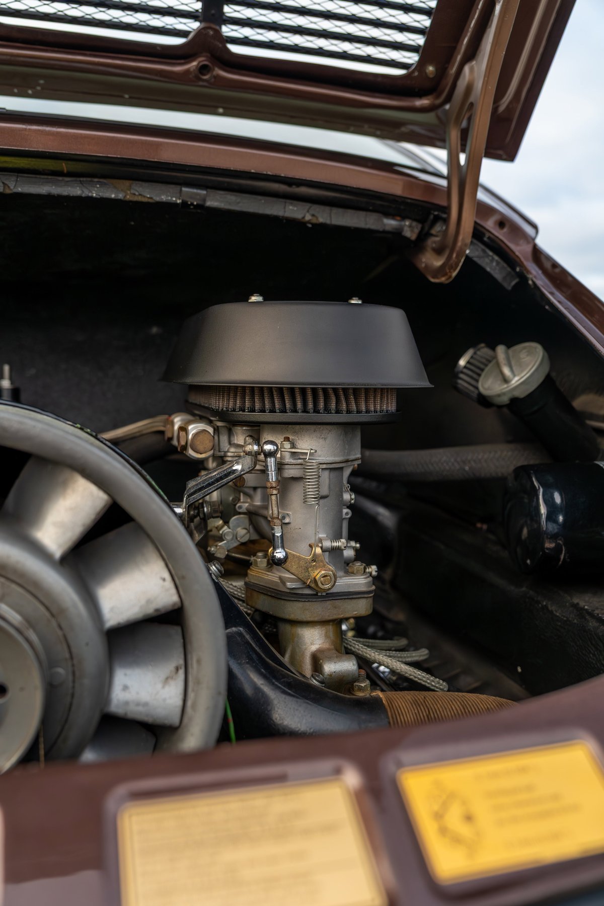 Detail shot of a 1975 Porsche 911 Carrera engine, showing a Weber carburetor and cooling fan.