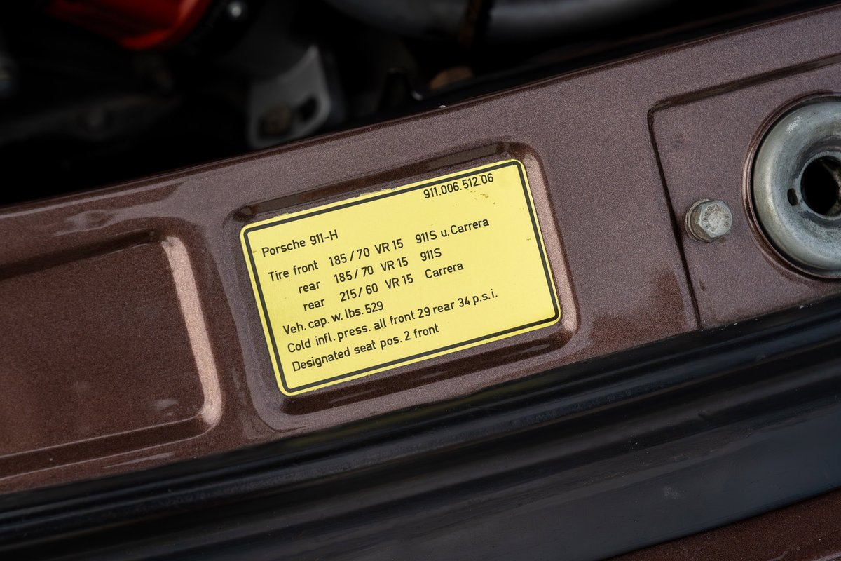 Close-up of a 1975 Porsche 911 Carrera tire pressure sticker on copper brown metallic paint.