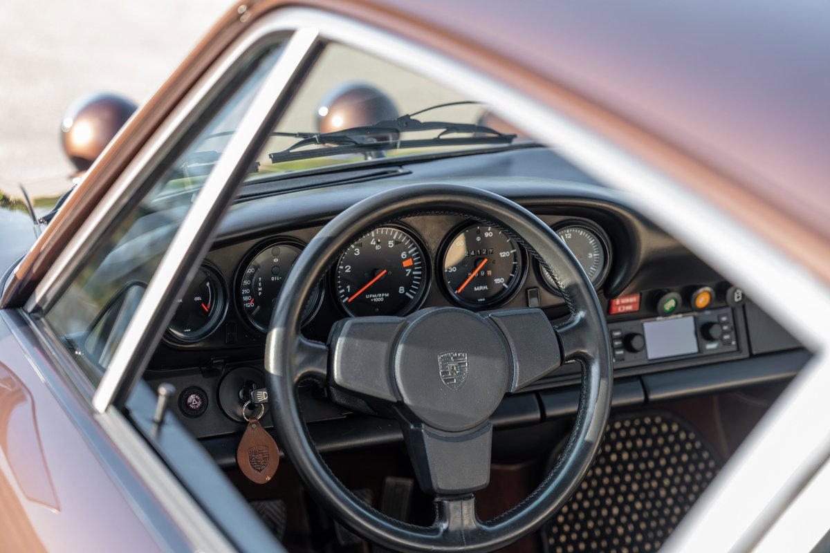 Porsche 911 Carrera interior with classic gauges, black steering wheel, and copper-brown metallic exterior trim.
