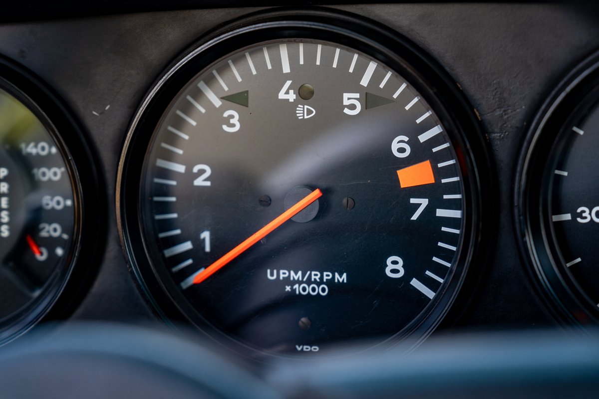 Close-up of a 1975 Porsche 911 Carrera tachometer, showing 6.5k RPM. Copper brown metallic paint.