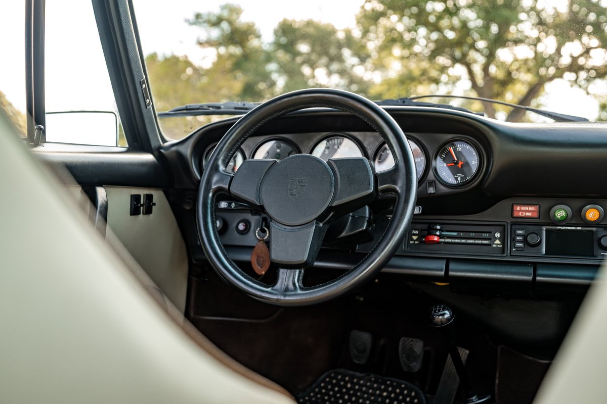 1975 Porsche 911 Carrera interior, featuring a black steering wheel and dashboard, analog gauges, and cassette deck.