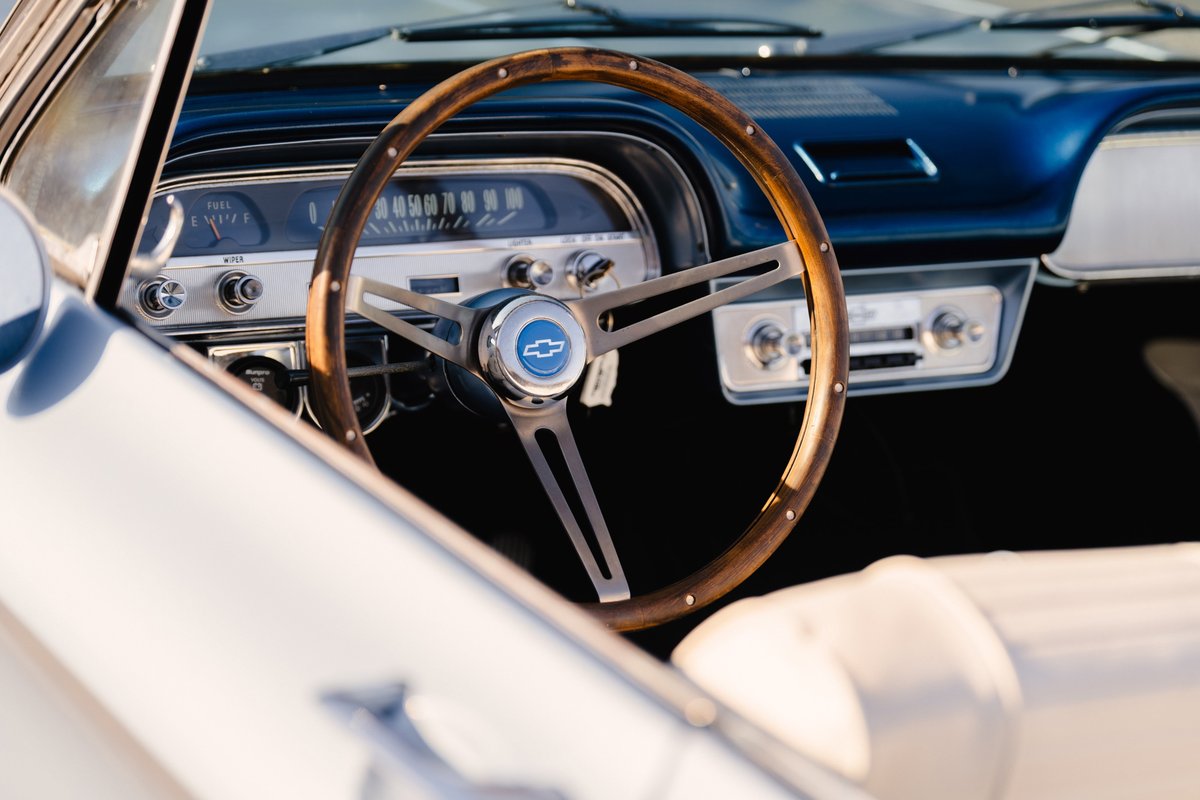 Close-up of a 1966 Chevrolet Corvair convertible interior. Features wooden steering wheel with bowtie emblem and retro radio.