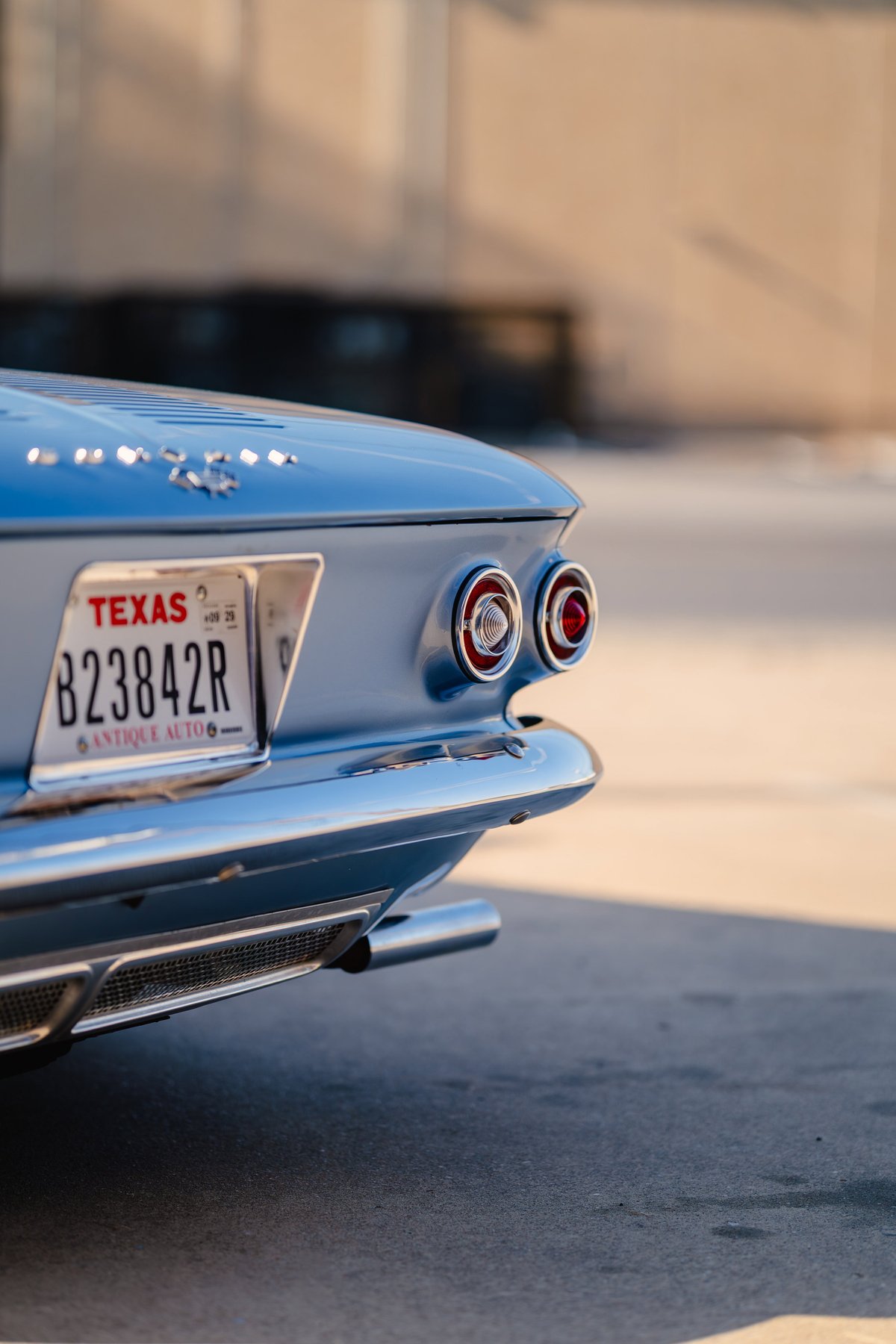 Rear view of a blue 1966 Chevrolet Corvair convertible with chrome trim and dual taillights.