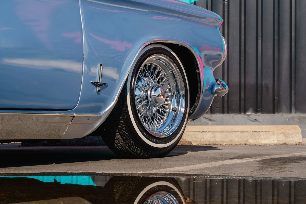 Close-up of a blue metallic 1966 Chevrolet Corvair convertible rear wheel, featuring chrome wire rims and whitewall tires.
