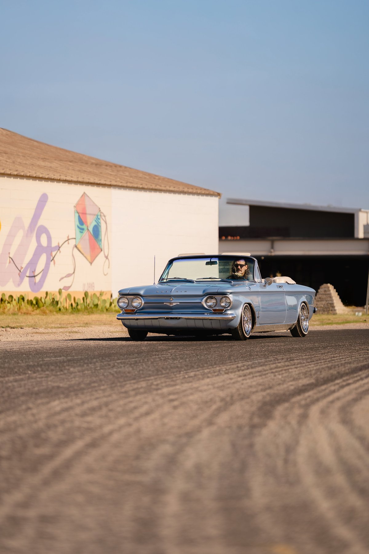 1966 blue metallic Chevrolet Corvair convertible with chrome trim and whitewall tires.