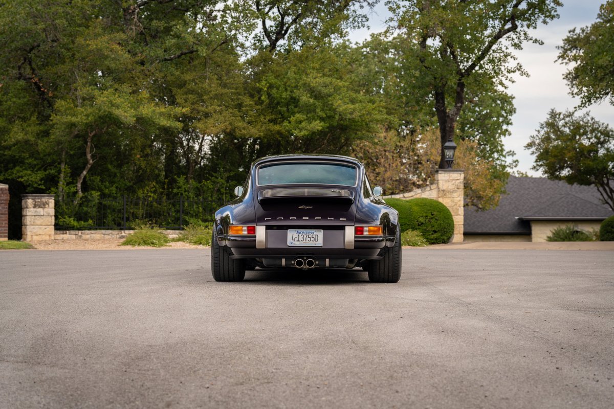 Rear view of an aubergine metallic 1990 Singer Porsche 911 with chrome trim and dual exhaust.