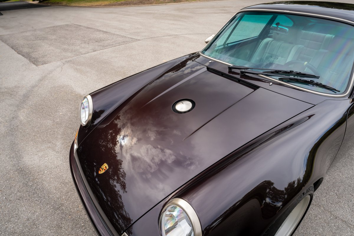 Front view of a 1990 Singer Porsche 911 in Aubergine Metallic. Classic headlights and hood trim.