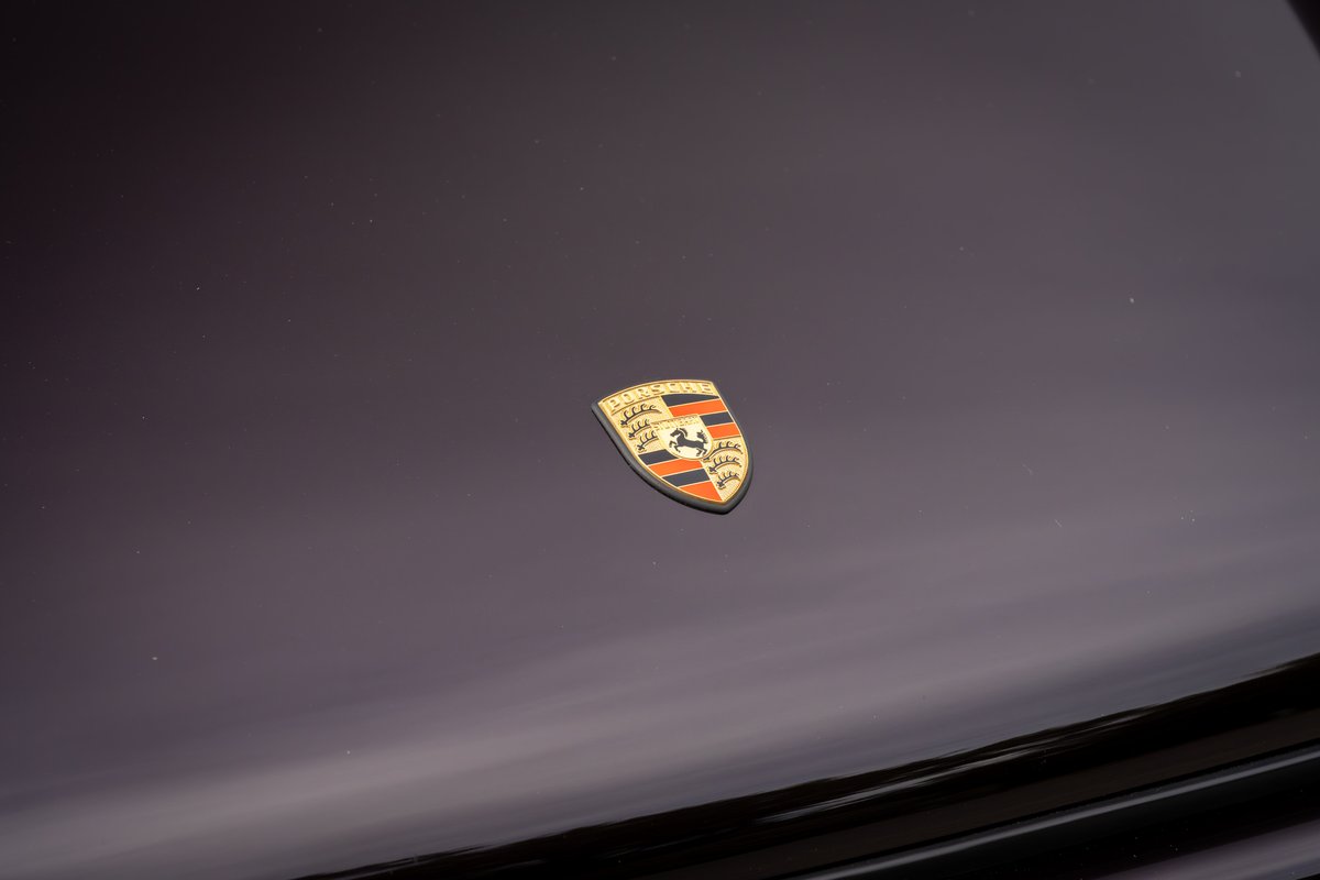 The Porsche crest emblem on the hood of an aubergine metallic 1990 Singer Porsche 911.
