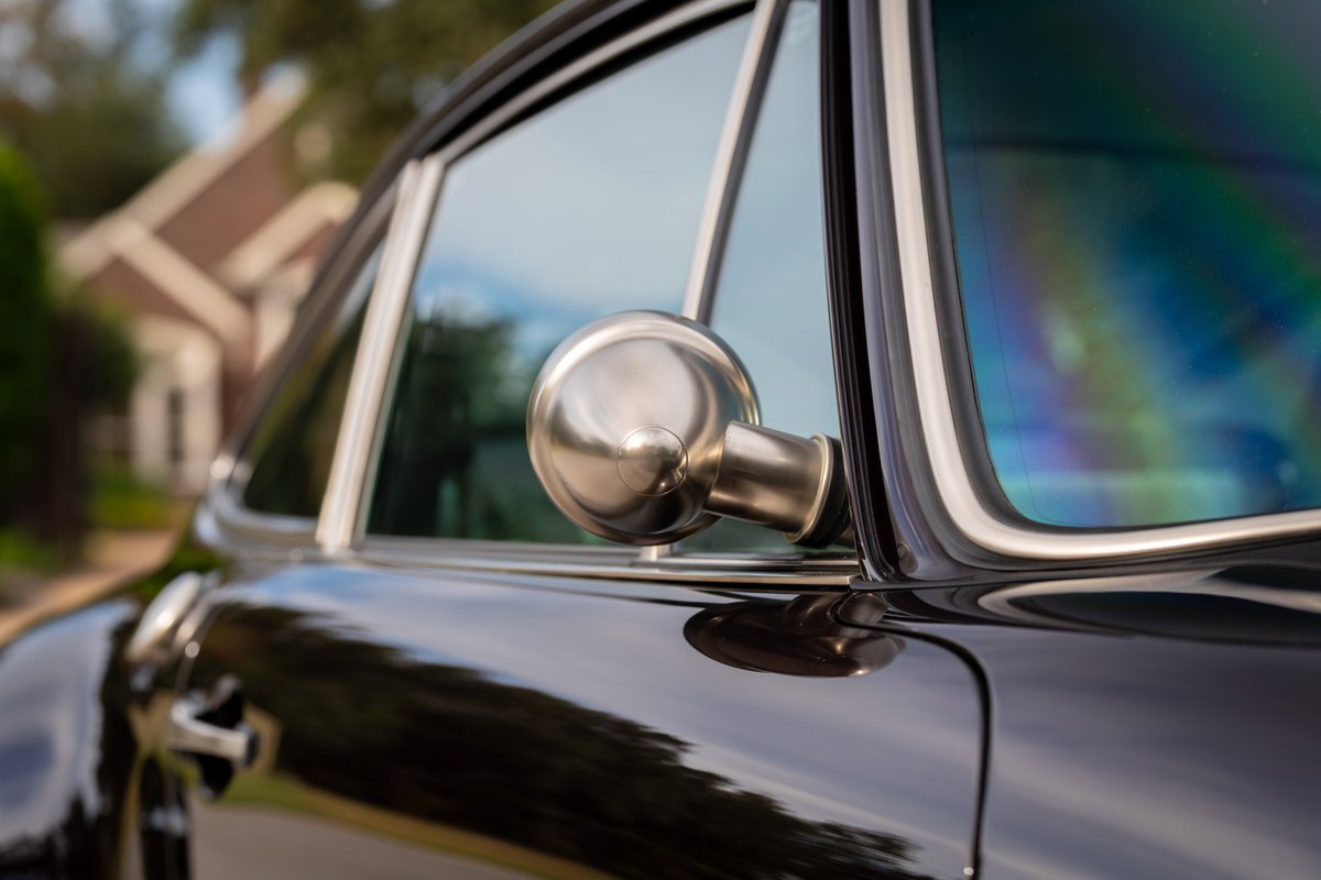 Closeup of a black 1990 Singer Porsche 911, showing the chrome side mirror and window trim.