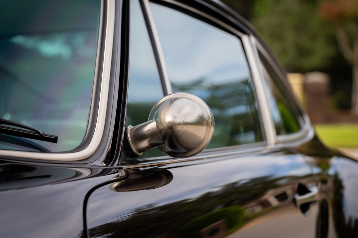 Close-up of a vintage aubergine metallic Singer 911 with chrome trim and a classic bullet side mirror.