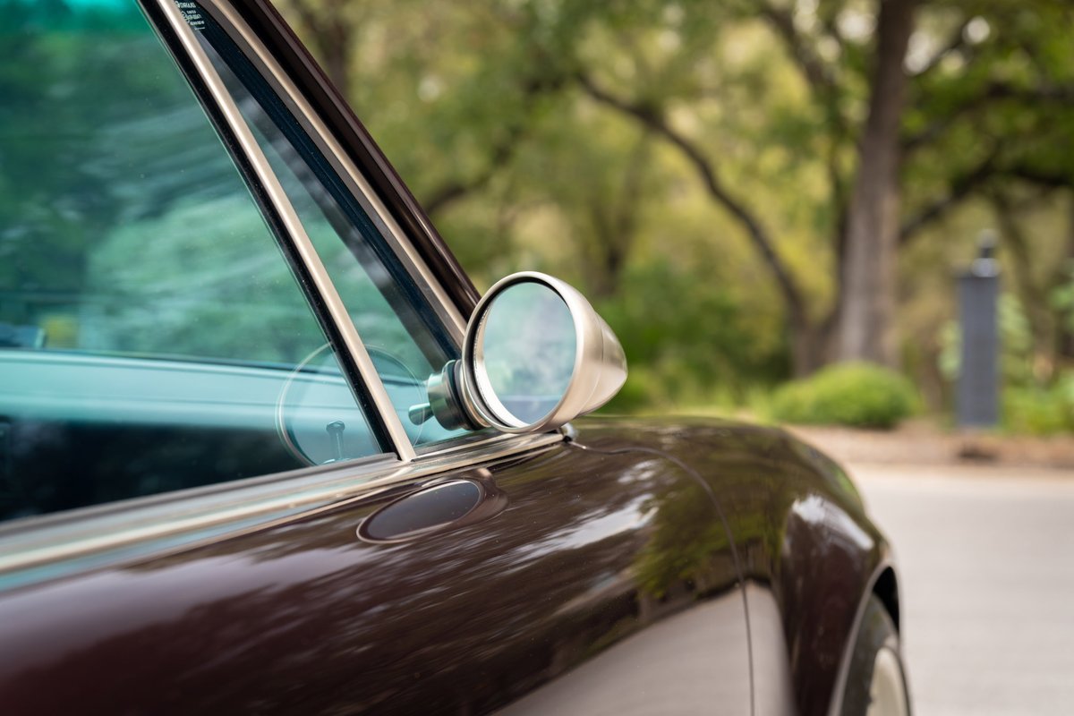 Detail of an aubergine metallic 1990 Porsche 911 Singer with chrome trim and side mirror.