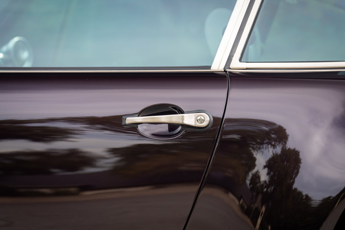 Close-up of a 1990 Singer Porsche 911 door in aubergine metallic paint, chrome trim, and chrome door handle.