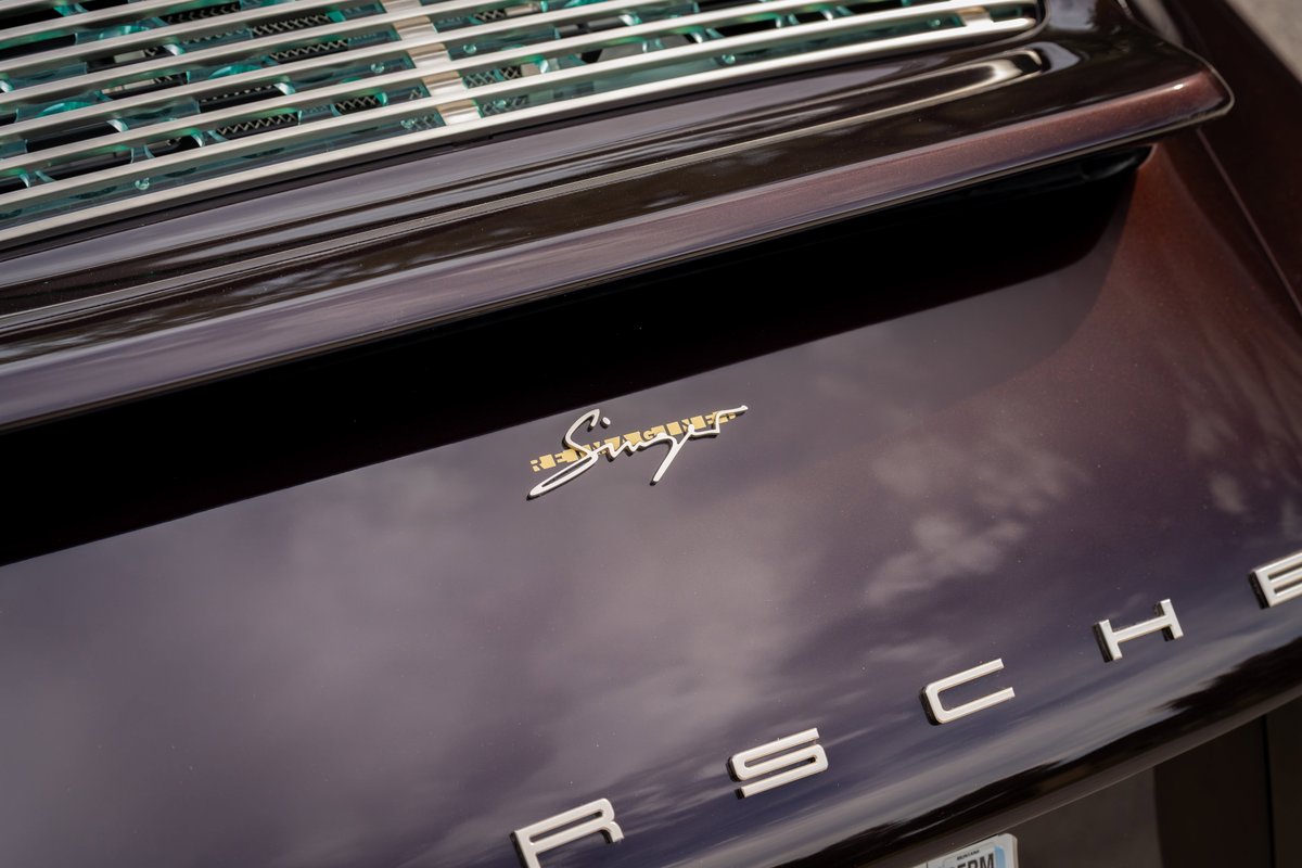 1990 Singer Porsche 911 in aubergine metallic. Close-up on gold Singer badging and chrome Porsche lettering.
