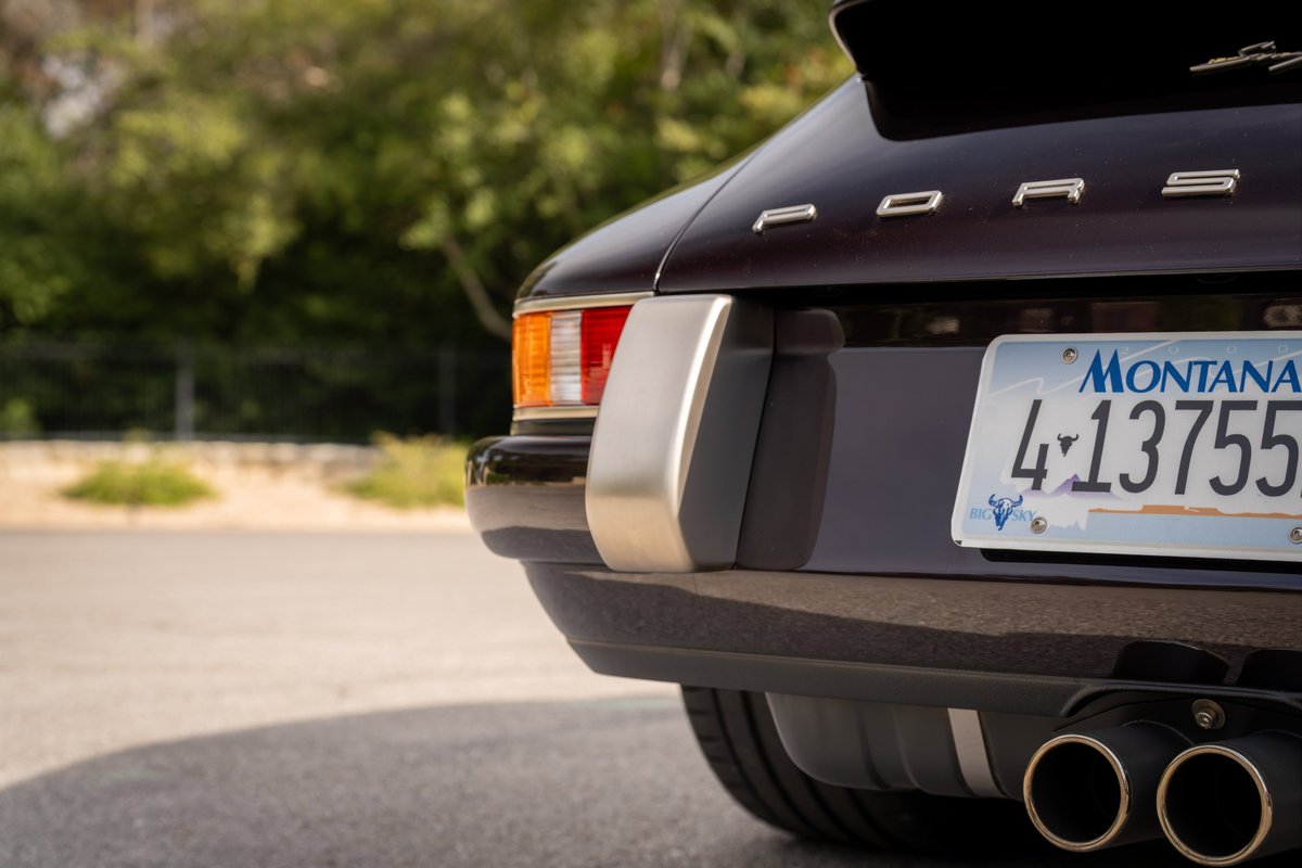 Rear view of an aubergine metallic 1990 Singer Porsche 911 with dual exhaust.