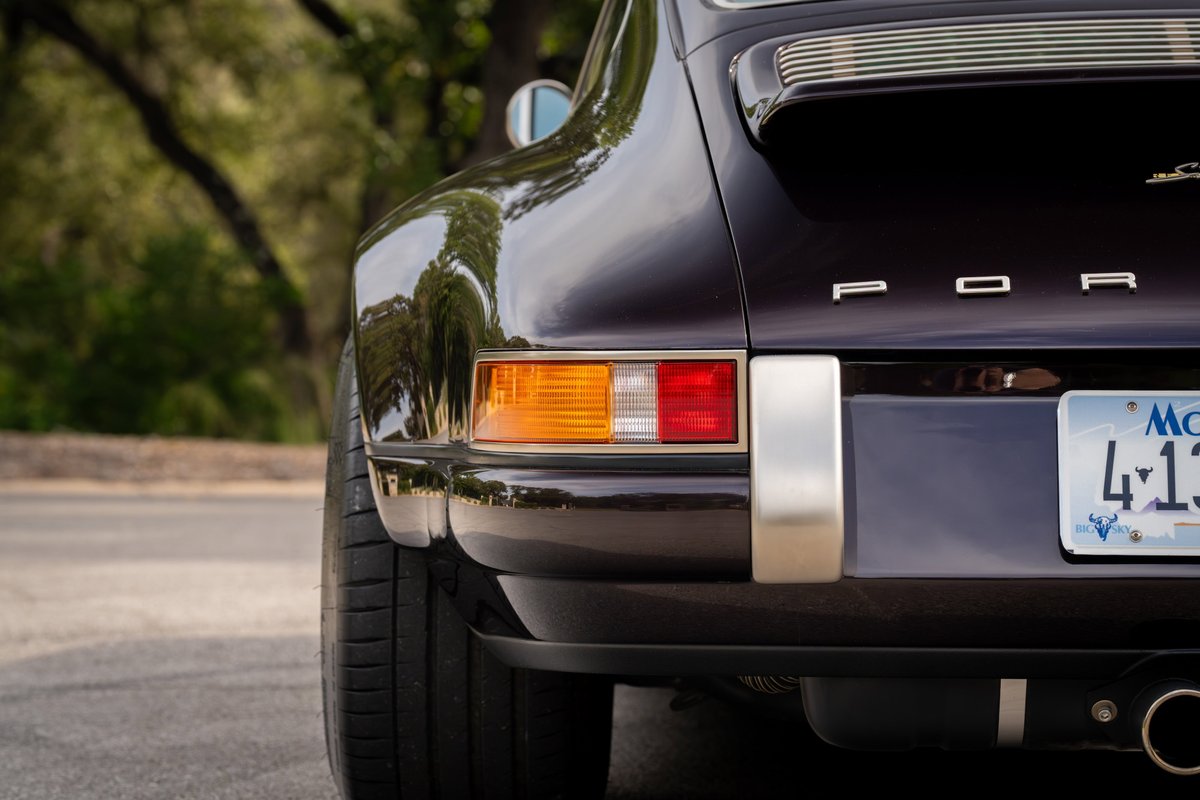 Close-up rear view of an aubergine metallic 1990 Singer Porsche 911, showing chrome trim and taillights.