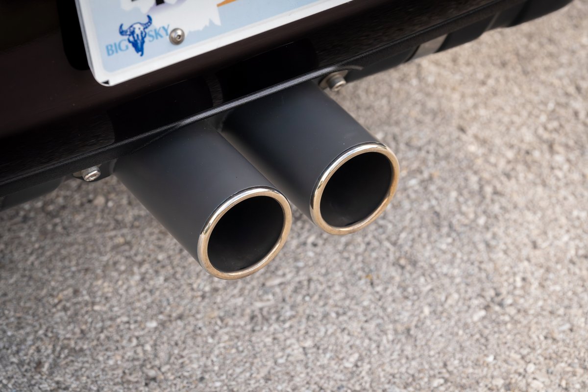 Close-up of dual matte black exhaust tips with polished chrome rims on an aubergine metallic 1990 Singer Porsche 911.