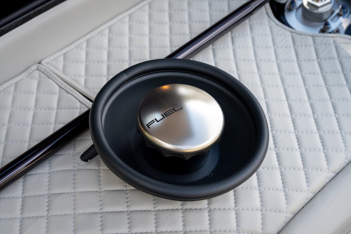 Close-up of brushed aluminum fuel cap with "FUEL" text on quilted white interior trim of a 1990 Singer Porsche 911.