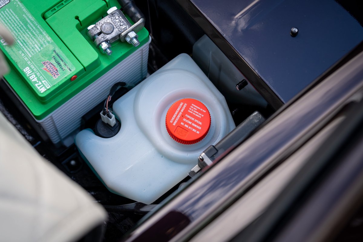 1990 Singer Porsche 911 engine bay: green battery, coolant reservoir, metallic trim.