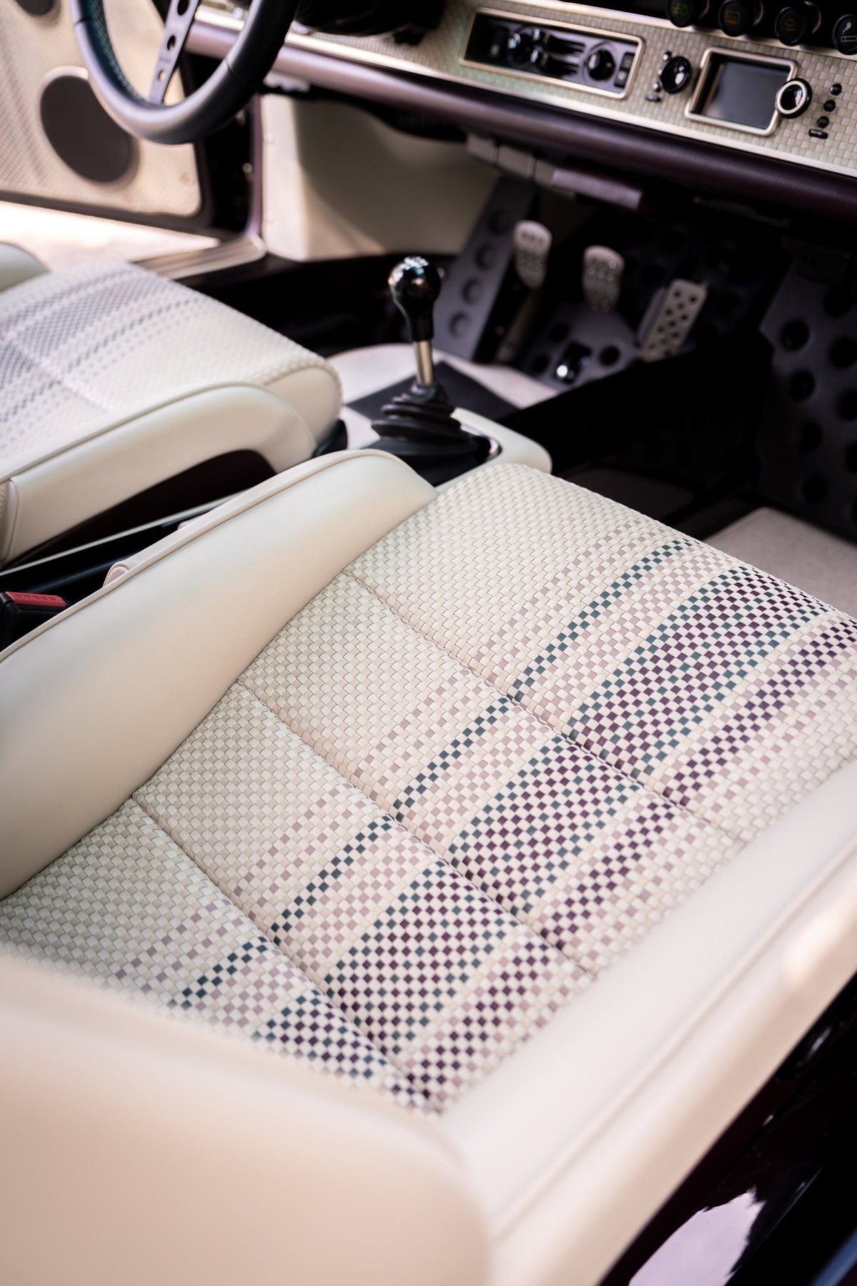 Interior of an Aubergine Metallic 1990 Singer Porsche 911, featuring tartan seat inserts and a gated shifter.