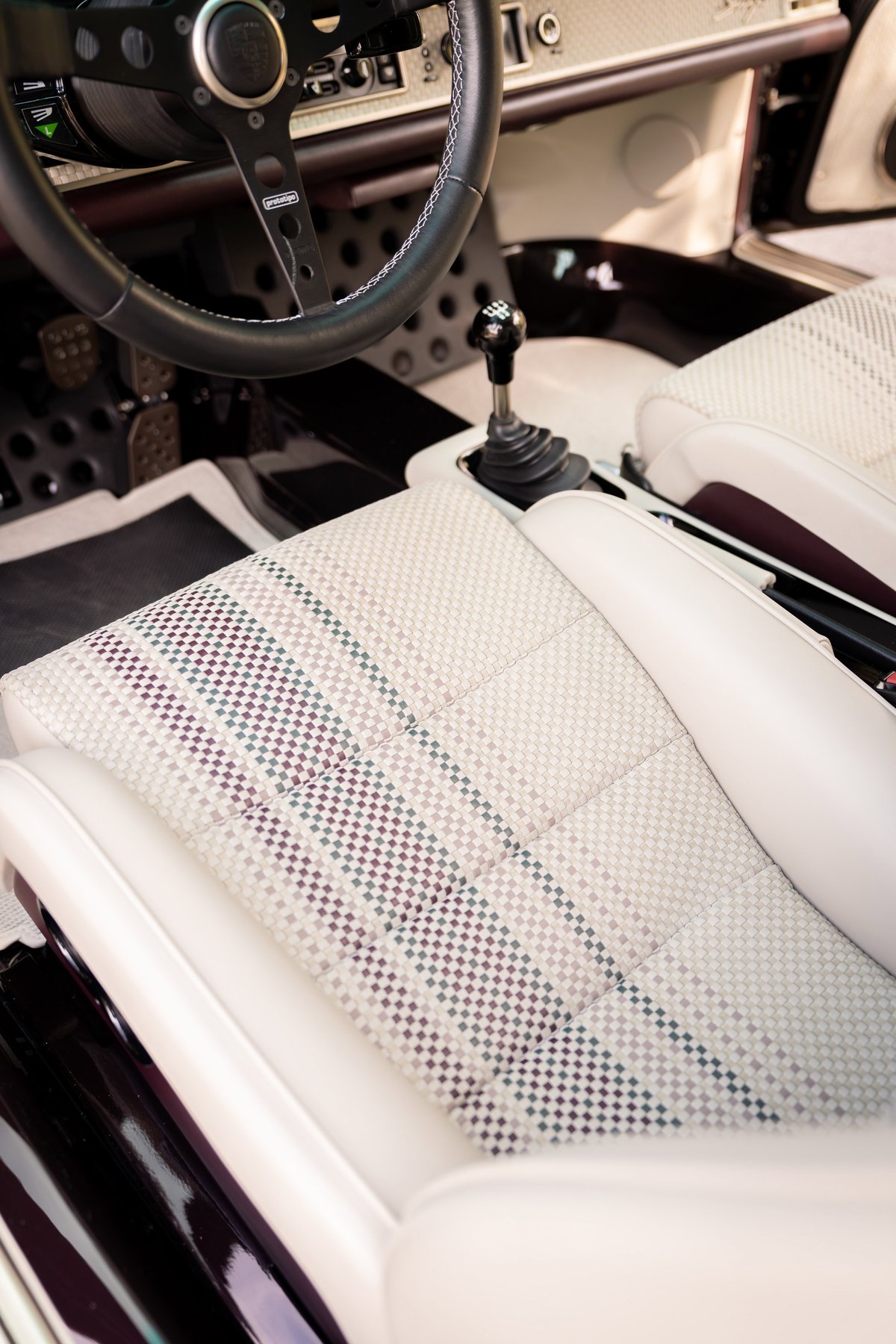 Close-up of aubergine metallic 1990 Singer Porsche 911 interior, checkered fabric seat trim