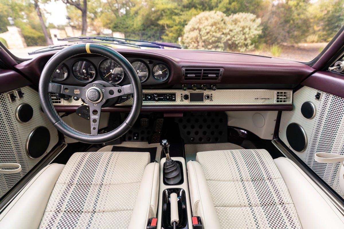 Interior view of an aubergine metallic 1990 Singer Porsche 911, featuring a classic steering wheel & plaid seats.