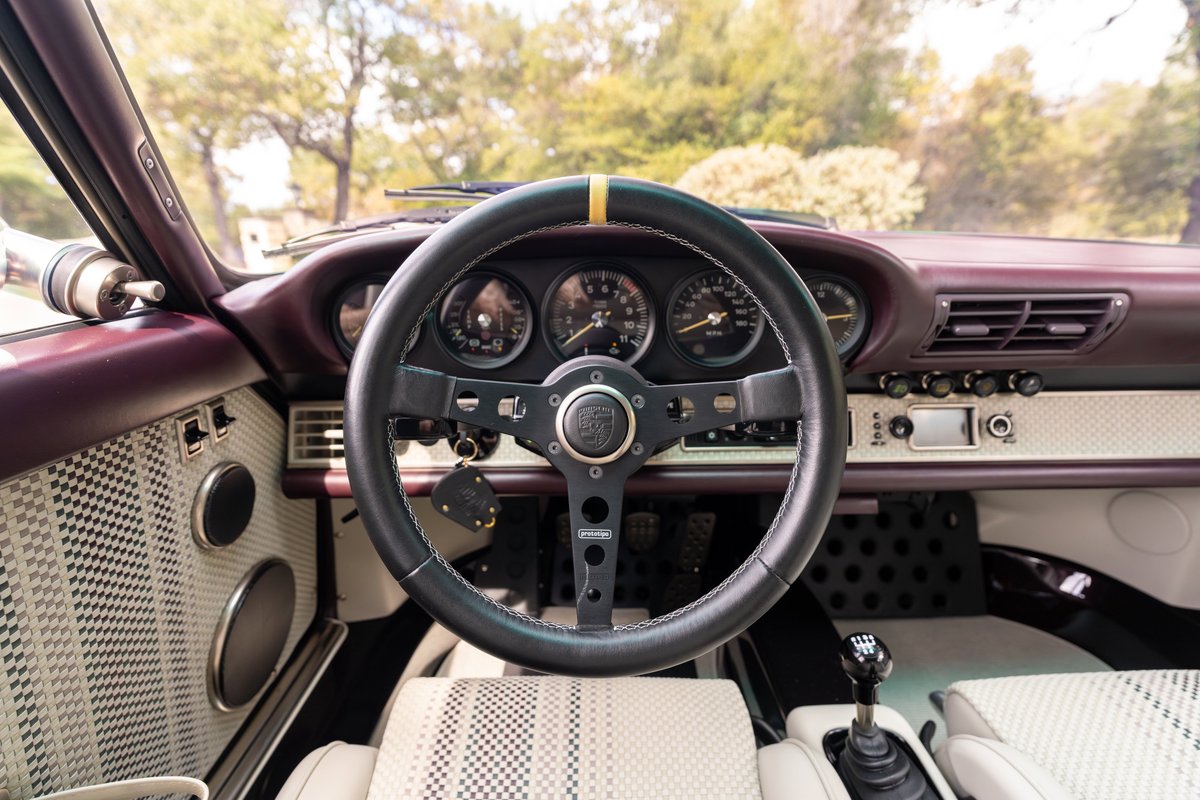 1990 Singer Porsche 911 interior: black steering wheel, aubergine trim, white diamond-pattern seats.