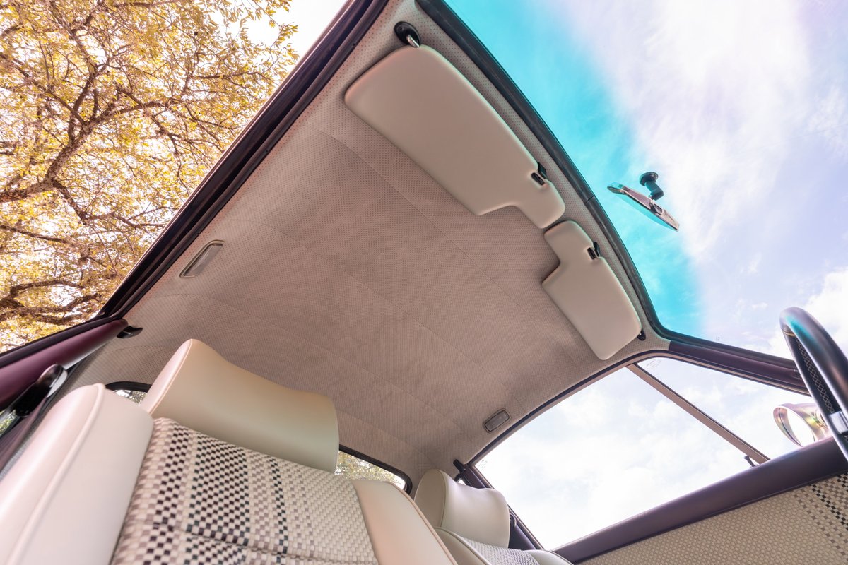 Interior view of aubergine metallic 1990 Singer Porsche 911 showing plaid seat inserts & sunroof.