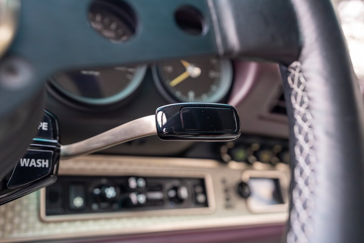 Close-up of the steering column stalk, tachometer, and dashboard controls of an aubergine metallic 1990 Singer Porsche 911.