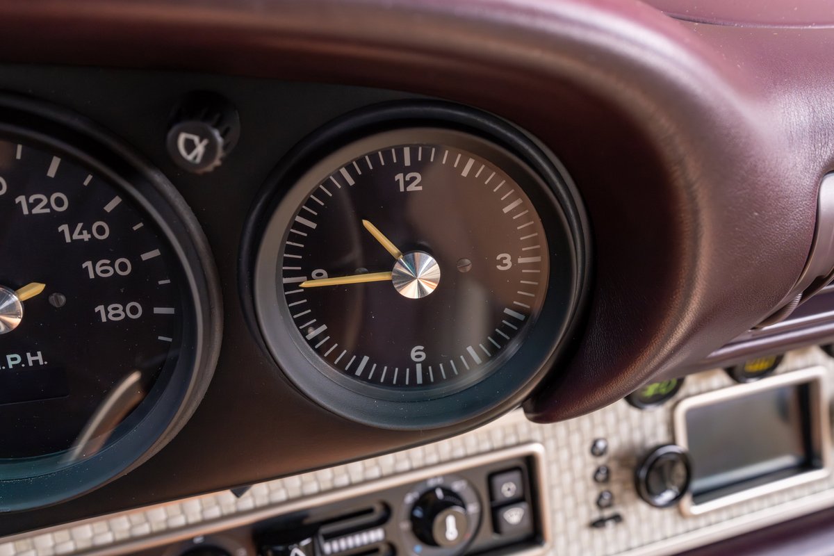Classic dashboard in a 1990 aubergine metallic Singer 911, featuring a tachometer and clock.