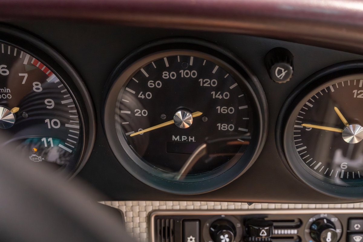 Close up of the dashboard in an aubergine metallic 1990 Singer Porsche 911, showing the tachometer and speedometer.