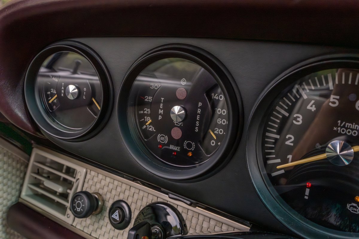 Close-up of a 1990 Singer Porsche 911 aubergine metallic dashboard, showing tachometer, oil pressure, and temp gauges.