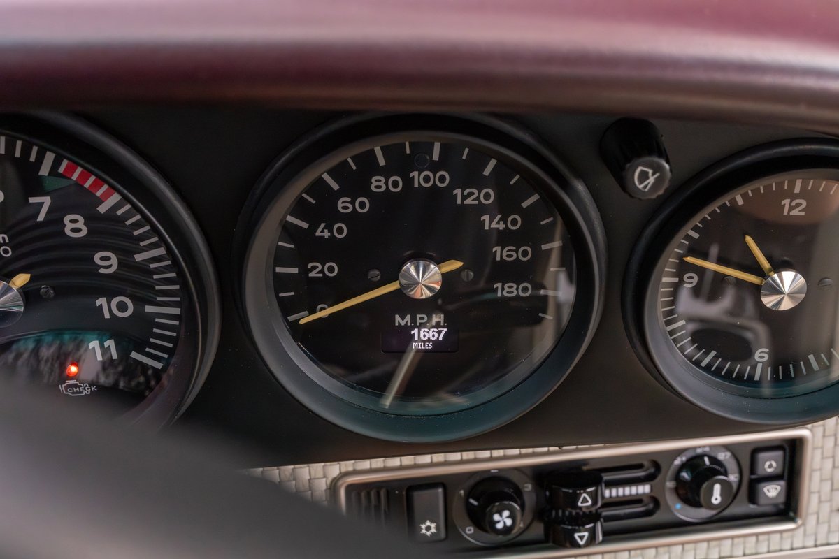 Close-up of aubergine metallic 1990 Singer Porsche 911 dashboard with analog gauges.