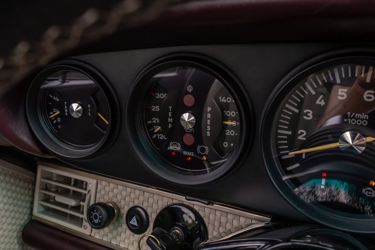Close-up of the instrument cluster in an aubergine metallic 1990 Singer Porsche 911, showing gauges and trim.