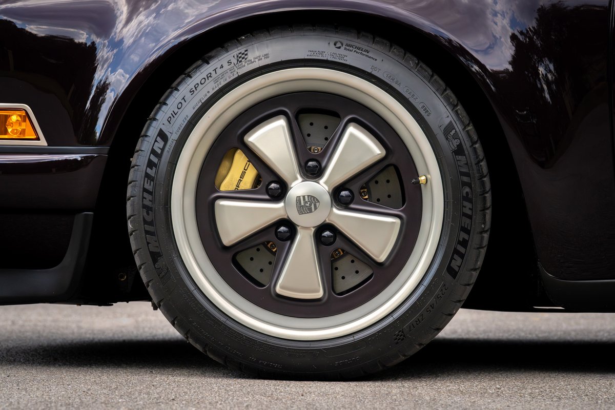 Aubergine metallic 1990 Singer 911 wheel with silver Fuchs rims, gold brake caliper, and Michelin tire.