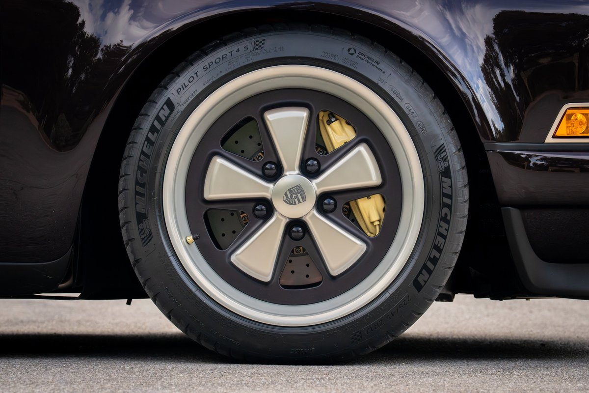 Close-up of an Aubergine Metallic 1990 Singer Porsche 911 wheel, with gold brake calipers and Michelin Pilot Sport tires.